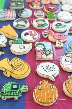 many decorated cookies sitting on top of a blue and pink table cloth with words written in different languages