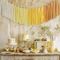 a table topped with cakes and desserts next to a wall covered in yellow streamers