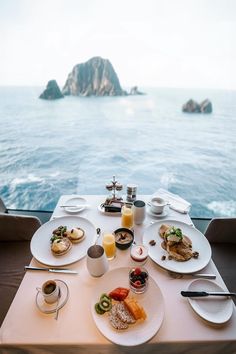 a table with food and drinks on it overlooking the ocean in front of an island