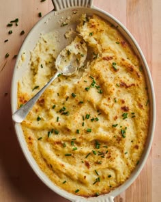 a white bowl filled with mashed potatoes on top of a wooden table next to a spoon