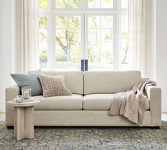 a white couch sitting in front of a window next to a table with a blanket on it