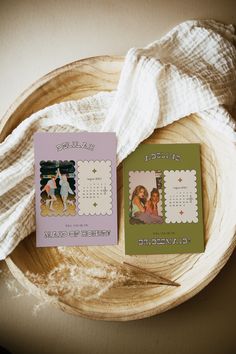 two small calendars sitting on top of a wooden bowl next to a white blanket