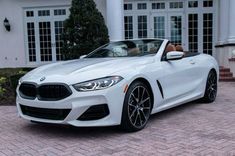 a white bmw convertible parked in front of a house