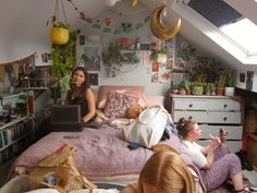 two women sitting on a bed in a room with lots of plants and other things