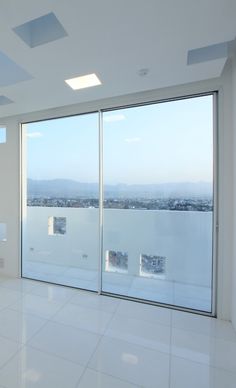 an empty white room with large windows and tiled flooring, overlooking the city below