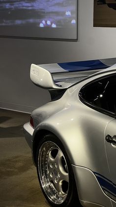 a silver sports car parked in front of a wall with pictures on it's side