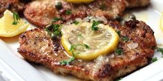 some meat with lemons and parsley on top of it in a white plate