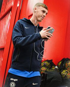 a young man listening to music while standing in front of a red wall