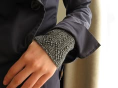 a person wearing a black jacket and silver cuff on their wrist with a hand in the pocket