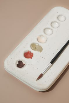 the paintbrush is next to an assortment of buttons on a white tray with a brown background