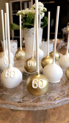 some cake pops with numbers on them sitting on a glass platter next to flowers