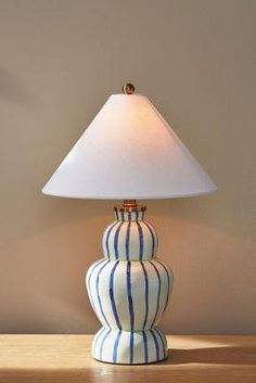 a blue and white striped lamp sitting on top of a wooden table next to a wall