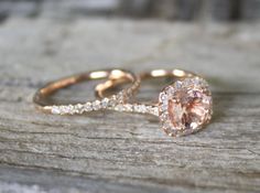 two gold rings with an oval pink diamond in the center on top of a piece of wood