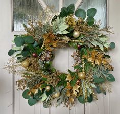 a wreath is hanging on the front door with greenery and gold ornaments around it