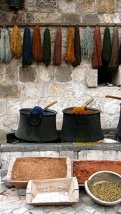 several pots and pans are lined up on a stone surface with spices hanging in the background