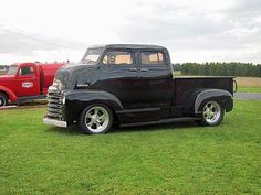 an old black truck parked on top of a lush green field