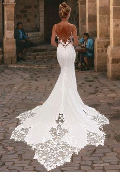 a woman in a white wedding dress is walking down the street with her back to the camera