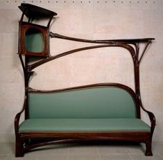 an old fashioned wooden couch with green upholstered seat and armrests, against a white wall