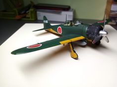 a green and yellow model airplane sitting on top of a white table next to a stack of books