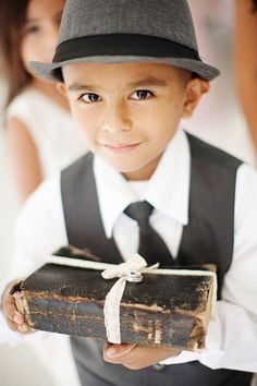 a young boy in a suit and tie holding an old book with a hat on it