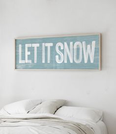 a wooden sign that says let it snow on the wall above a bed