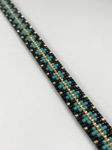 a blue and gold bracelet on a white table with a black beaded cord in the middle