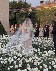 the bride and groom are standing in front of white flowers, surrounded by other people