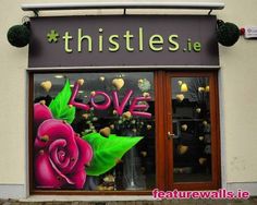 a storefront with flowers painted on the front and side windows that say thistles ie