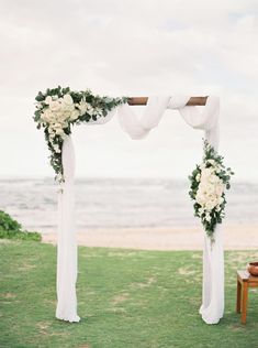 an outdoor wedding ceremony setup with white flowers and greenery on the grass by the ocean