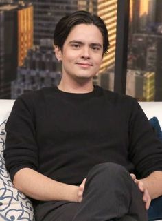 a man sitting on top of a white couch in front of a cityscape