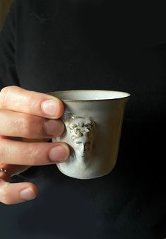 a person holding a white cup with a lion head on it's side in their left hand