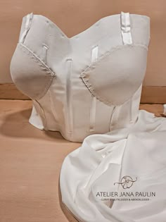 a white corset sitting on top of a wooden floor next to a pillow