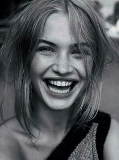 a smiling woman with blonde hair and blue eyes is posing for a black and white photo