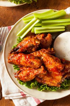 a white plate topped with wings, celery sticks and mashed potato wedges