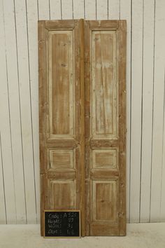 an old wooden double door with chalkboard on the bottom and bottom panel, in front of a white wall