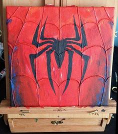 a spiderman painting on an easel in front of a wooden cabinet with drawers