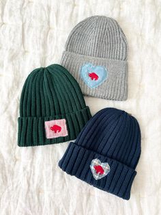 three knitted hats with hearts on them sitting on a white sheet in the bed