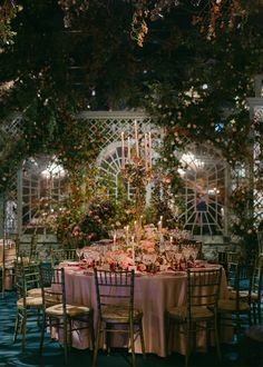 a table set up for a formal dinner with flowers and greenery on the walls