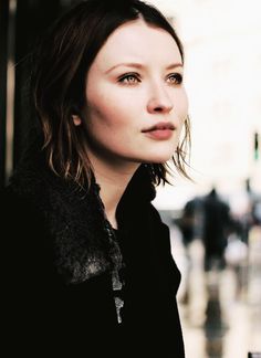 a woman standing in front of a building on a rainy day looking at the camera