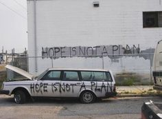 an old car parked in front of a building with graffiti on it's side