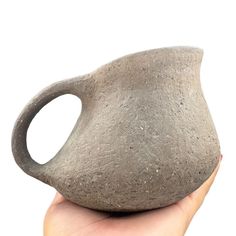 a hand holding a stone vase in front of a white background