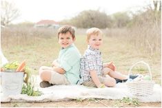 two young boys sitting on a blanket with vegetables