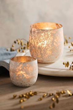 two white candles sitting on top of a table next to gold flakes and other decorations