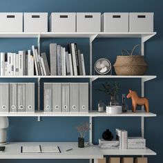 a white shelf filled with lots of books and binders next to a vase on top of a table