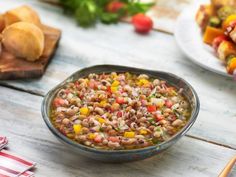 a bowl filled with beans and vegetables on top of a wooden table next to bread