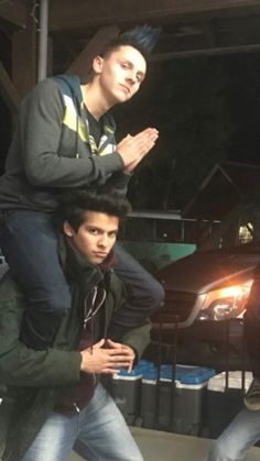 two young men standing next to each other in front of a car with their arms around one another