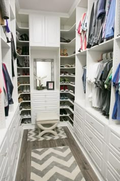 a walk - in closet with white cabinets and shelves filled with clothes, shoes and other items