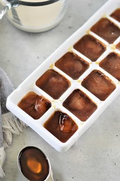 an ice cube tray filled with brown liquid next to a bowl of milk and spoons