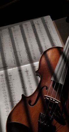 an old violin laying on top of sheet music with the sun shining through it's shadow