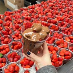 a person holding up a cup with chocolate and strawberries on it in front of rows of plastic containers